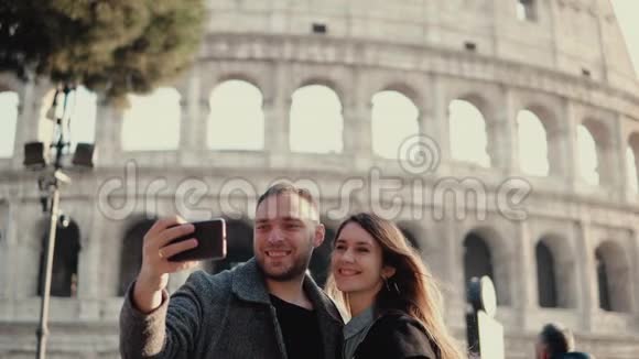 年轻的幸福夫妇在意大利罗马旅行男人和女人在竞技场附近的智能手机上拍照视频的预览图