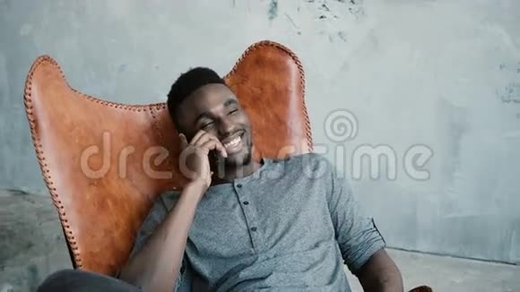非洲男人坐在椅子上用智能手机说话的肖像男人在开玩笑玩得很开心视频的预览图