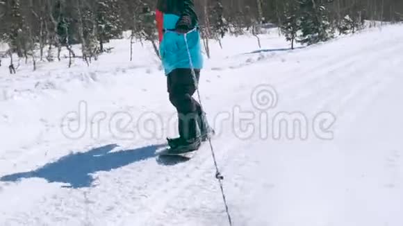 在一个阳光明媚的冬天在雪山上骑着一条绳子穿着颜色鲜艳的夹克和太阳镜的快乐男子滑雪板视频的预览图