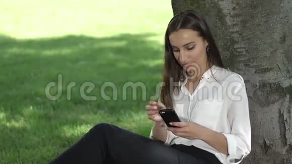 女商人在公园的树下检查手机视频的预览图