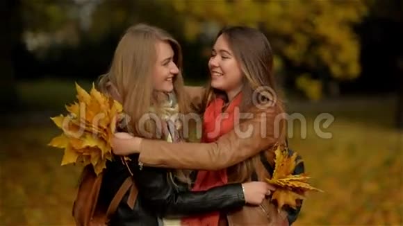 两个美丽的少女在秋天的公园里拥抱和捧着一束黄叶女朋友在里面玩视频的预览图