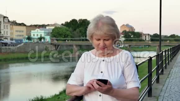 傍晚时分在海滨老城区河桥附近使用智能手机的老年妇女视频的预览图