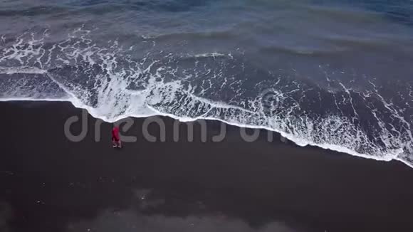 鸟瞰一个穿着红色裙子的女孩在沙滩上走着黑色的沙子西班牙加那利群岛特内里费视频的预览图