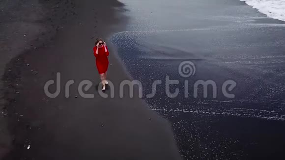 鸟瞰一个穿着红色裙子的女孩在沙滩上走着黑色的沙子西班牙加那利群岛特内里费视频的预览图