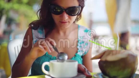 戴着太阳镜在海滩咖啡馆吃早餐燕麦片的漂亮女孩1920x1080视频的预览图