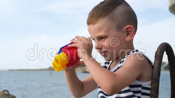 穿着条纹衬衫的可爱小男孩透过双筒望远镜看海视频的预览图