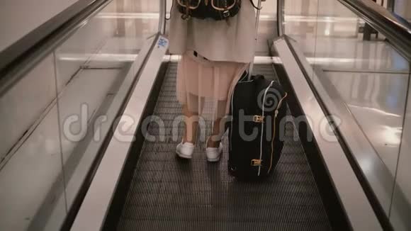 站在自动扶梯上的带手提箱的年轻一双漂亮的女足在机场视频的预览图