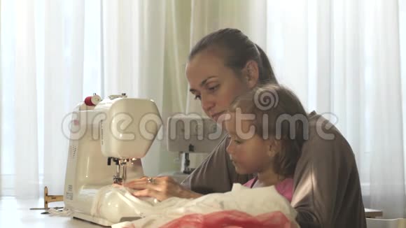 年轻漂亮的母亲和她可爱的小女儿一起在缝纫机上工作视频的预览图