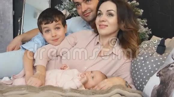有儿子和新生儿的年轻家庭在圣诞节躺在床上视频的预览图