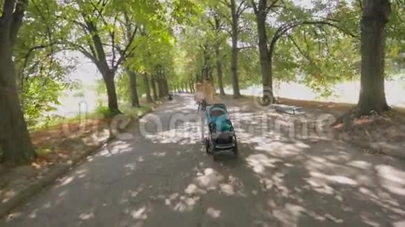 快乐的年轻妈妈搂着小儿子在公园里和婴儿车散步视频的预览图
