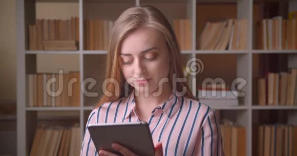 在大学图书馆里用平板电脑拍摄年轻漂亮的白种人女学生的特写照片视频的预览图