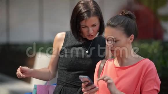 两位时尚色彩鲜艳的购物者带着袋子在街上购物带着智能手机视频的预览图