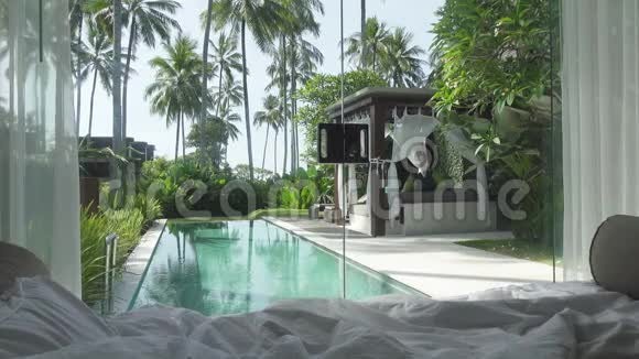从游泳池的卧室和带有棕榈树的热带花园可以看到风景视频的预览图