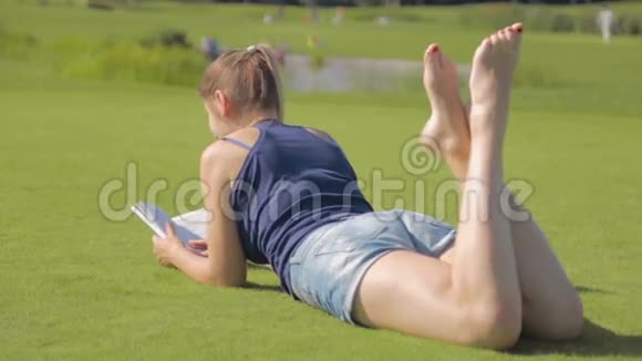 一位长腿的年轻女子躺在公园的草地上看书视频的预览图