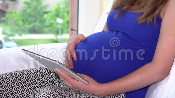 大肚子孕妇坐在窗边用平板电脑视频的预览图