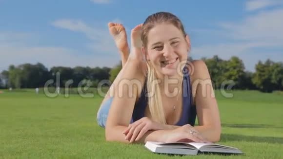 在大学公园的草地上躺着一本书的快乐微笑女孩多莉拍摄视频的预览图