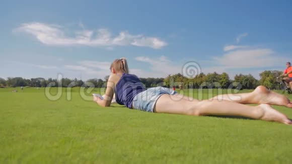 一个长腿的小女孩躺在公园的草地上看书视频的预览图
