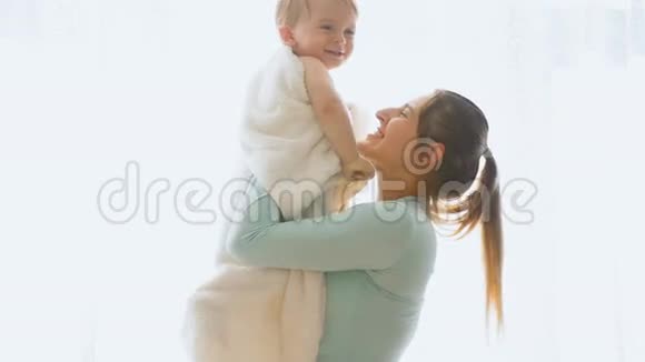 快乐的年轻母亲在大窗户拥抱她的小儿子的慢镜头视频的预览图