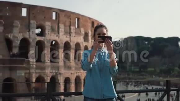 一位年轻的旅游女性在意大利罗马的斗兽场拍照智能手机微笑着笑着慢动作视频的预览图