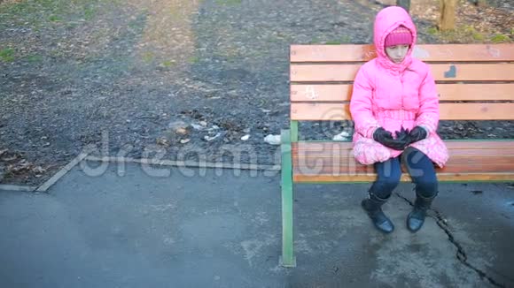 秋天坐在长凳上伤心的小女孩在公园里视频的预览图