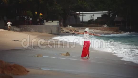 快乐的黑发女人戴着帽子在海滩上奔跑1920x1080视频的预览图