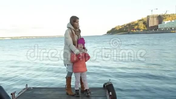 一个女人带着一个女孩一个母亲带着一个女儿站在河港上牵手拥抱微笑快乐视频的预览图