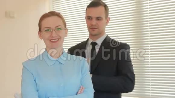 两个商人正站着微笑着看着摄像机在办公室里的背景上写着声明视频的预览图