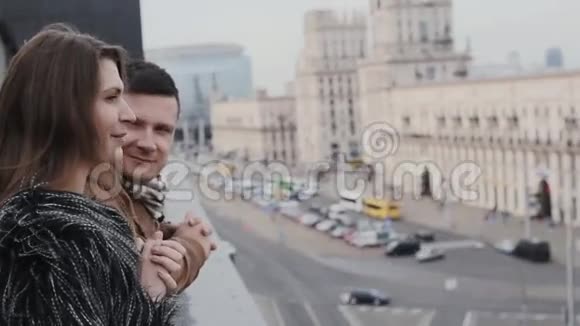 一位漂亮的年轻女子和一位英俊的黑发男子在一旁交谈从屋顶欣赏城市街道的景色视频的预览图