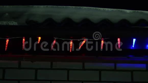 多种颜色的圣诞灯在晚上装饰房子在冬天的屋顶上闪闪发光的花环雪在屋顶上视频的预览图