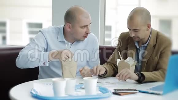 两个商人在午餐时讨论这个项目两个商人吃着中国面条讨论一个商业计划视频的预览图
