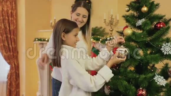 年轻微笑的母亲和女儿在客厅装饰圣诞树的画像视频的预览图