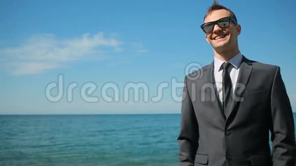 商人穿着西装在海滩上散步看着镜头微笑视频的预览图