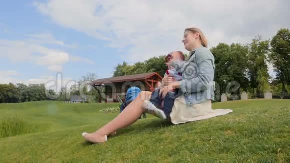 快乐的年轻母亲在公园的草地上拥抱和玩耍她的小儿子视频的预览图
