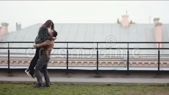 男人把心爱的人抱在怀里在屋顶上旋转快乐的恋人在寒冷的天气里一起玩视频的预览图
