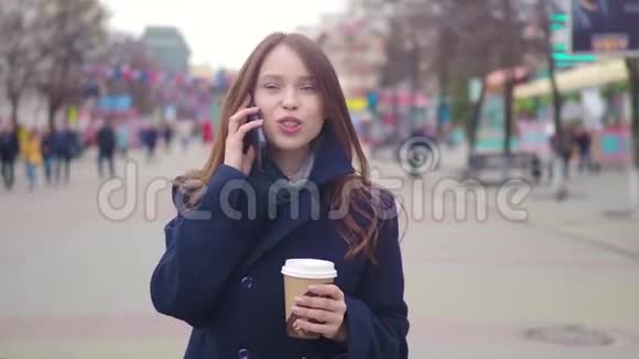 多莉拍摄了一个迷人的混血女孩在城市街道上说着智能手机喝着咖啡散步年轻女子视频的预览图