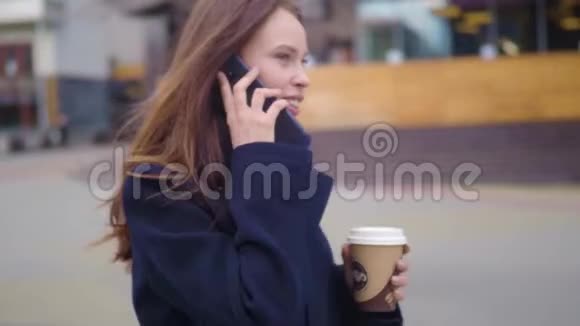 多莉拍摄了一个迷人的混血女孩在城市街道上说着智能手机喝着咖啡散步年轻女子视频的预览图