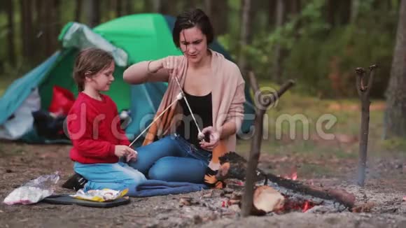 幸福的家庭在大自然中有美好的时光妈妈教女儿在明火上煮棉花糖视频的预览图