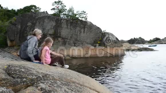 母亲和女儿坐在海边的大石头上视频的预览图