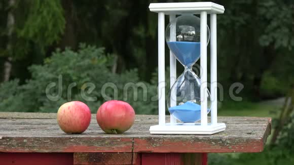 夏天用蓝色沙漏和旧桌子上的两个苹果结束静物视频的预览图