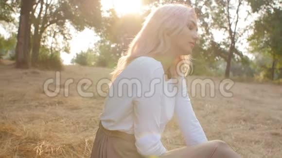 美丽的女孩坐在一片被阳光淹没的草地上穿着一件连衣裙浪漫的心情年轻的女人享受自然美视频的预览图