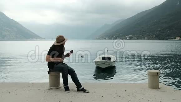 戴着帽子穿着破牛仔裤的女人坐在码头上弹吉他视频的预览图