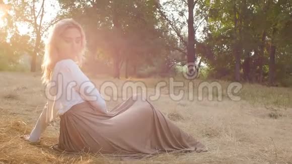 美丽的女孩坐在一片被阳光淹没的草地上穿着一件连衣裙浪漫的心情年轻的女人享受自然美视频的预览图