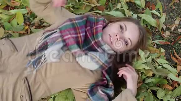 一个穿着外套躺在秋叶上的年轻女子开心地笑着视频的预览图