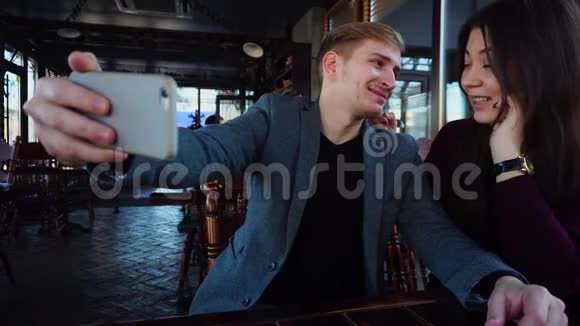 女朋友和男朋友坐在咖啡馆里用智能手机自拍视频的预览图