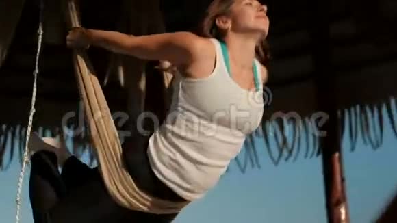 在阳光明媚的海滩上一个女人以飞行姿势在吊床上摆动视频的预览图
