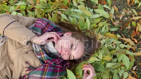 一个穿着外套躺在秋叶上的年轻女子开心地笑视频的预览图