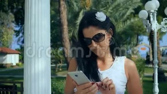 女人在热带花园的智能手机上打字假期视频的预览图