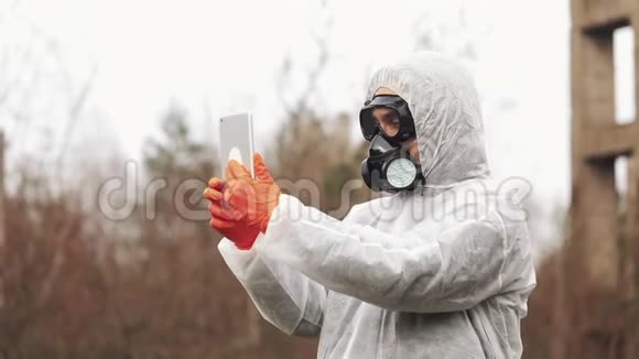 穿着生物危险服和防毒面具的人在被污染的土地上的平板电脑上记笔记视频的预览图