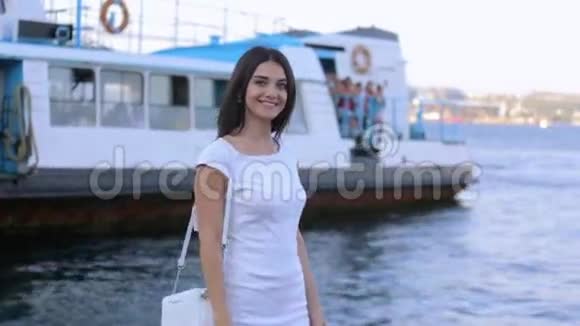 穿着白色连衣裙在海边的码头上散步的美丽的黑发女郎视频的预览图