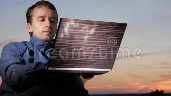 日落时分一个年轻人在笔记本电脑后面工作后面是美丽的天空视频的预览图